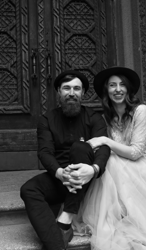 extraordinary-wedding-couple-dressed-hats-formal-outfits-is-sitting-stone-stairs-smiling